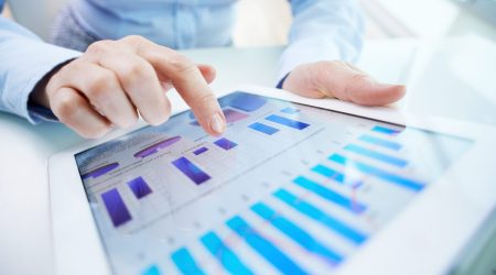 Image of human hand pointing at touchscreen with business document