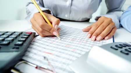 Photo of human hands holding pencil and ticking data in documents